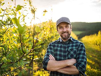 Mann steht mit verschränkten Armen, im Hintergrund Landschaft