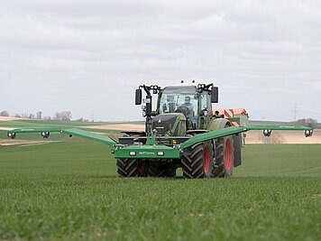 Ein Traktor düngt eine Wiese mit einem Düngerstreuer und den NEXT Farming Green Seeker.