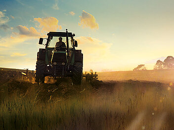 Traktor fährt über das Feld bei Sonnenuntergang und warmer Lichtstimmung